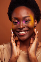 pretty young african american woman with curly hair posing cheerful gesturing on brown background, lifestyle people concept