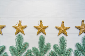 Fototapeta na wymiar Green spruce branches stacked in a row with Christmas toys golden stars on a light background with copy space
