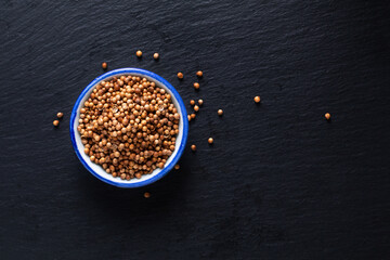 Food ingredient concept organic coriander seed in ceramic bowl on black slate stone board with copy space