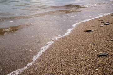 Small pebbles and wet sand on the sea beach; water line. Calm transparent water.