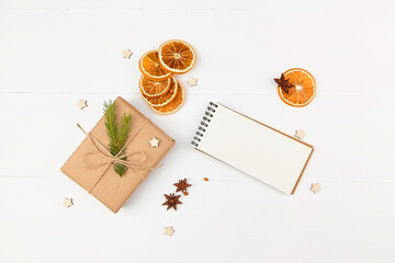 Christmas flat lay with gift box, spices, oranges and blank notepad on white background.