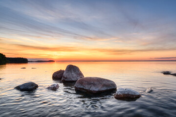 Fototapeta na wymiar Summer sunset over Lake Onega in Karelia. Stones in the water against the background of the sunset sky.