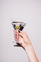 cropped view of woman holding glass of martini with olive on white - obrazy, fototapety, plakaty
