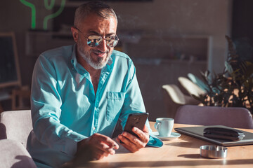 Man drinking morning coffee and smoking while looking at his phone.