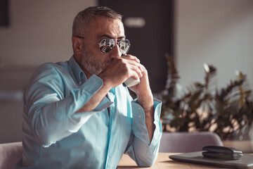 Middle aged man drinking morning coffee and smoking on his job break in a cafe.