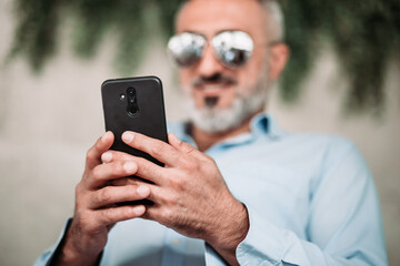 Man with beard and with sunglasses looking at the phone. Focus on the phone. Communication technology