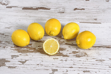 High angle shot of a sliced lemon placed in a white wooden surface and surrounded with 5 whole ones