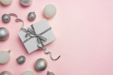 Gift box, silver decorations and ornaments on pastel pink background. Christmas background. Flat lay, top view, copy space.