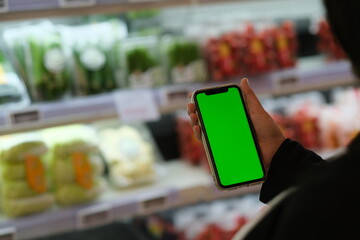 over shoulder view of people holding green screen smart phone in grocery store. Blur background