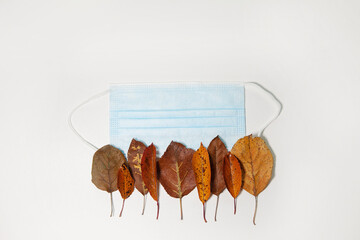 Multicolored autumn leaves and medical mask on white background. Concept of Thanksgiving day, Coronavirus outbreak situation. Flat lay, top view, copy space