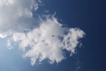 A helicopter flies in the distance against the background of white clouds.
