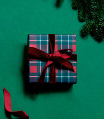 Christmas or New Year concept greeting card with a stylish tartan pattern gift box and velvet ribbon on the dark green background. Top view