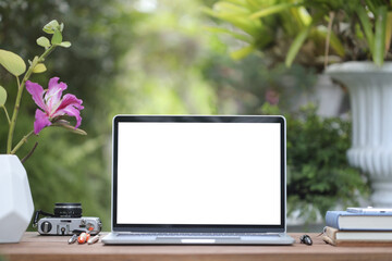 Laptop blank white screen with notebokks and flower pot on brown wooden table outside
