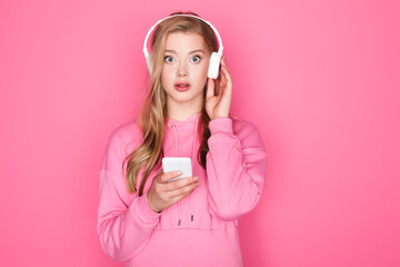 shocked beautiful woman in headphones with smartphone on pink background