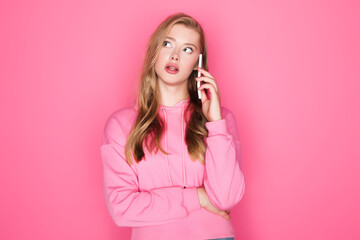 pensive beautiful woman talking on smartphone on pink background