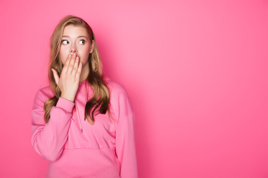 Shocked beautiful woman covering mouth on pink background