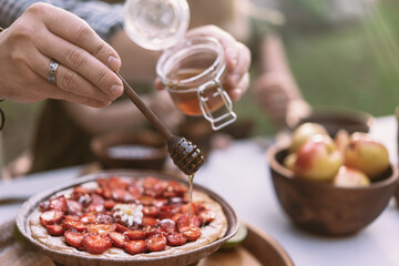 Hand pouring honey on strawberry pie in the garden