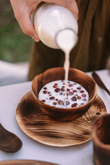 Girl's hand pours milk from a bottle into a wooden plate with strawberries in the garden
