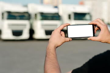 Mock up of a smartphone in the hands of a man. Against the backdrop of trucks. Logistics concept.
