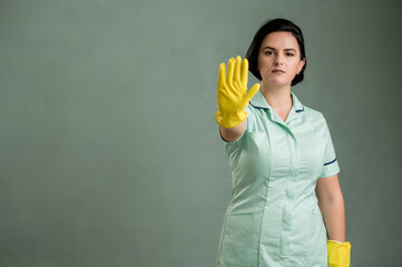 Young cleaning woman wearing a green shirt and yellow gloves showing stop sign