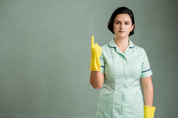 Young cleaning woman wearing a green shirt and yellow gloves counting one with her finger