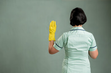 Young cleaning woman wearing a green shirt and yellow gloves showing oath from behind