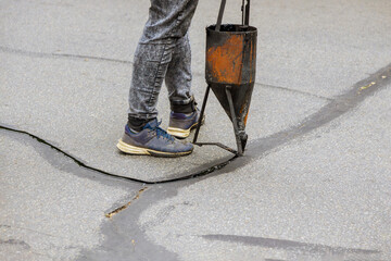 Workers restoration work sealing cracks applying liquid sealer to asphalt a road protective coat on...