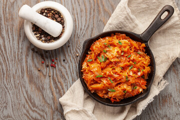 Stewed cabbage in skillet on wooden background in rustic style. Top view