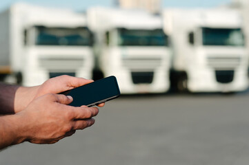 Mock up of a smartphone in a man's hand. Against the backdrop of trucks. Logistics concept.