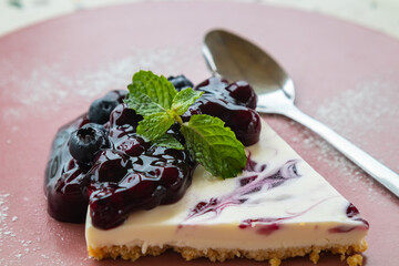 Piece of blueberry cheesecake on ceramic plate with peppermint leaves on top.