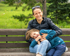 A happy caucasian woman and caucasian boy laughing and having fun while sitting on a bench in the street. 