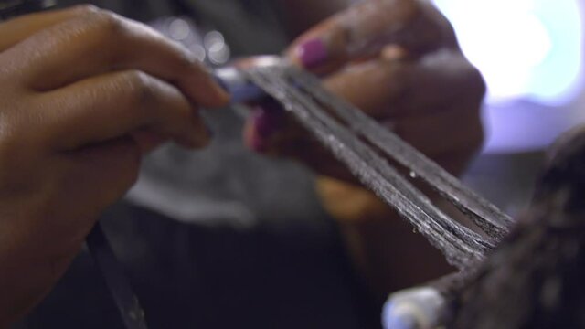 Close up of African hairstylist's hands rolling a perm roller into her customer's hair at a hairdressing salon.
