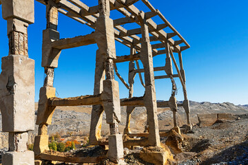 Fototapeta premium Old industrial bridge in the mountains. Destroyed mountain bridge. Abandoned concrete bridge. Concrete piles. Karatau mountains. Mountain stones. Blue sky. Mining Industrial Plant Bridge