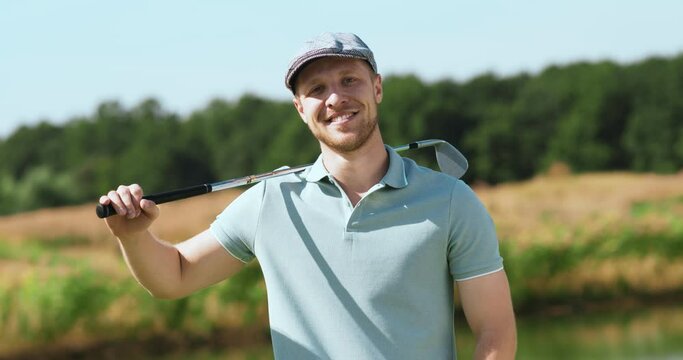 Outdoor portrait of young bearded man posing with golf stick, smiling to camera, tracking shot