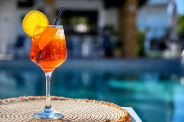 Red cocktail with orange slice and ice near a hotel pool