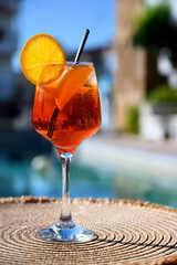 Red cocktail with orange slice and ice near a hotel pool