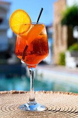 Red cocktail with orange slice and ice near a hotel pool