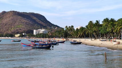 Fototapeta na wymiar Fishing boats near Front Beach. Coastline of Vung Tau. Sea, palm trees and hill. Vietnam. South-East Asia