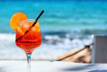 Red cocktail with orange slice and ice on a sea background