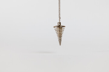 Gold metal pendulum on a white background. Holistic and energetic elements.