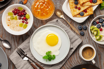 Continental breakfast captured from above (top view, flat lay). Coffee, tea, croissants, jam, egg, pancakes, maffins and oatmeal. Wooden background. Family breakfast table.