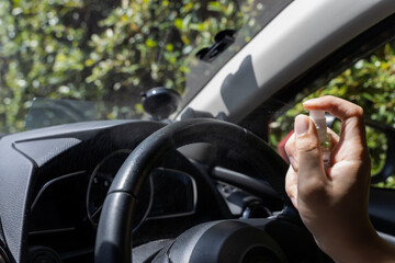 Human hand using alcohol spray to disinfect steering wheel in the car. Spraying prevent infection of coronavirus Covid-19.