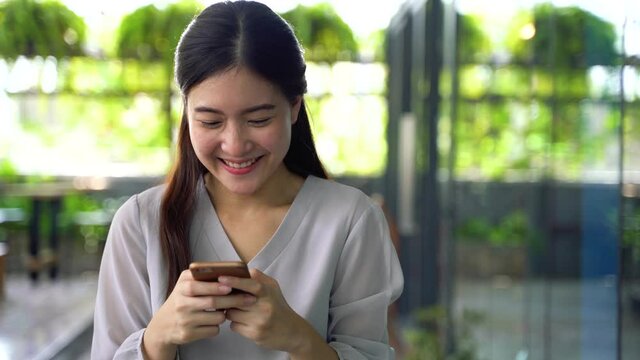 Young 20s Asian pretty girl holding a mobile phone in window glass building scene. Online and internet technology happiness concept