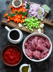 Ingredients for preparing beef stew - beef fillet, tomato sauce, red wine, vegetables on a dark background, top view