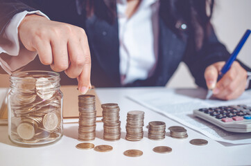 Closeup image businesswoman holding coins putting to stacking coins bank and calculating. concept...