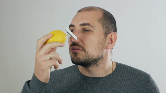 The man does not smell and taste, the sense of smell is lost, the symptoms of coronavirus. Man with a clothespin on his nose trying to smell the lemon