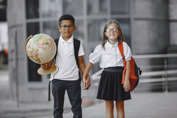 Mixed-races boy and little girl. Junior students in front of school. Pretty Caucasian girl. African American cute boy in white t-shirt. Pupils concept