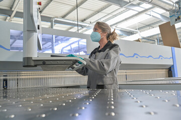 Female engineer is operating on a digital pannel in the company and wearing protections against...
