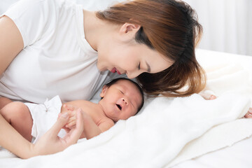 Beautiful asian women mother long hair in the white pajamas. mom kiss at newborn infant with love, while a baby sleeping in her arm with warm, safe, comforted resting on the clean bed.