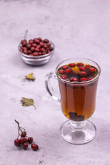 Healthy hawthorn berry tea in a glass and a handful of berries in a glass bowl on a concrete background
